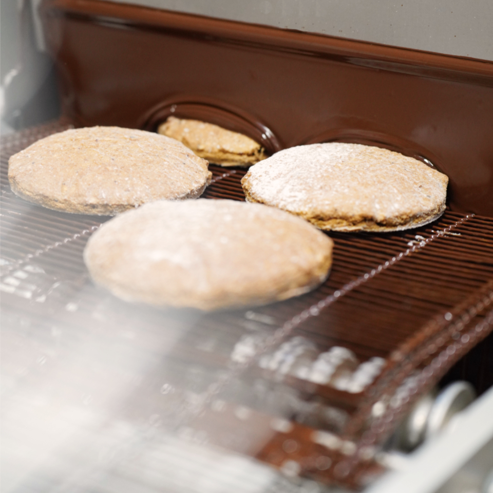 Elisenlebkuchen werden auf einem Fließband mit dunkler Pralinenschokolade überzogen