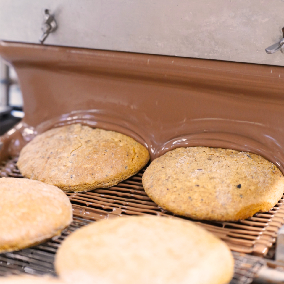 Elisenlebkuchen werden auf einem Fließband mit Vollmilch Pralinenschokolade überzogen