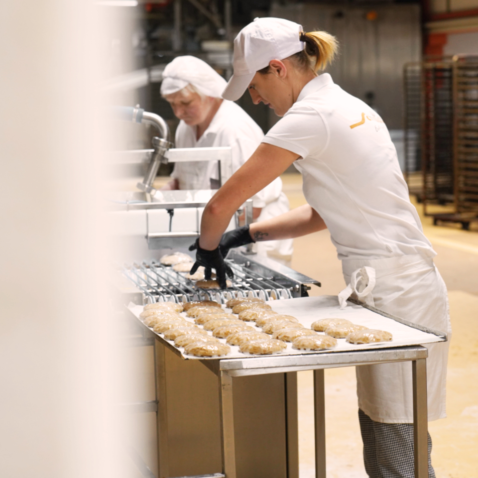 Elisenlebkuchen werden von 2 Personen nach dem glasieren vom Band genommen und auf einem Tablett platziert