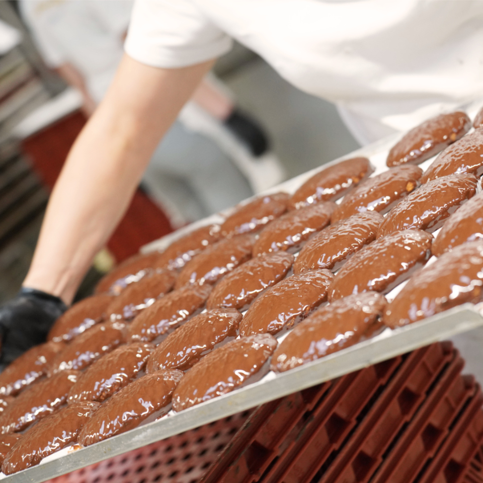 Elisenlebkuchen mit dunkler Pralinenschokolade werden von einer Person zum trocknen in den Regalwagen geschoben