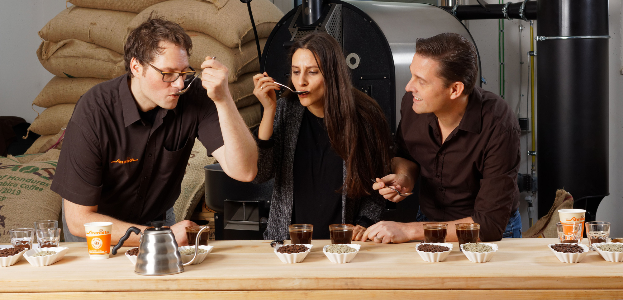 Drei Personen sitzen an einem Tisch und kontrollieren verschiedene Kaffeesorten