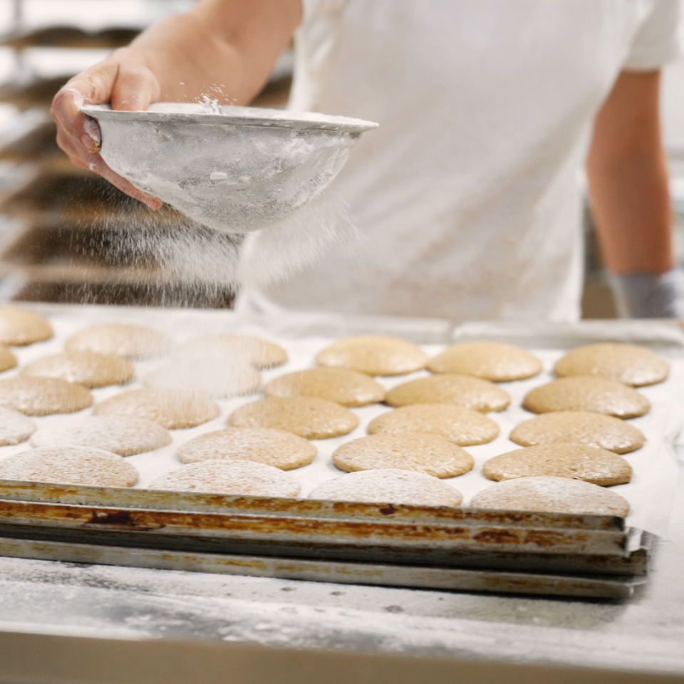 Elisenlebkuchen liegen auf einem Tablett auf einem Tisch und werden von einer Person mit Puderzucker bestäubt